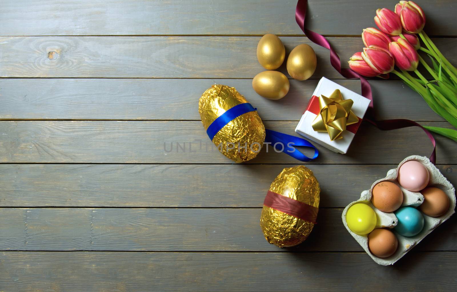 Gold easter eggs with spring tulips and gift box on a wooden table 