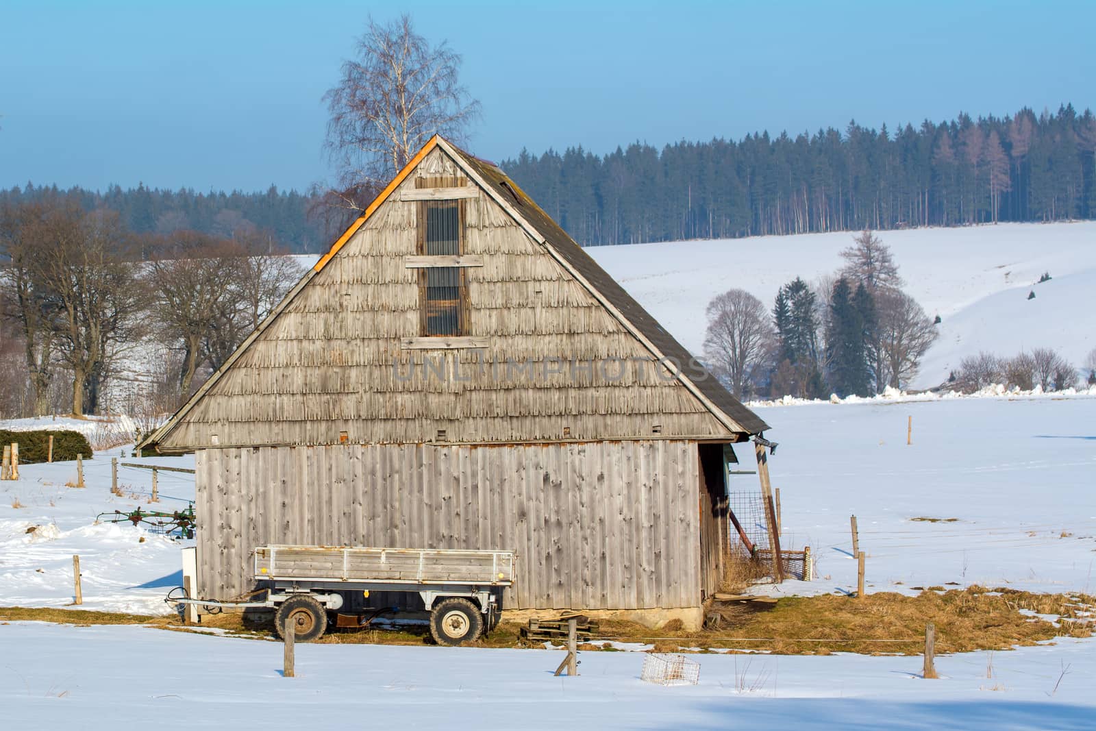 Old wooden barn with a wagon in the winter landscape