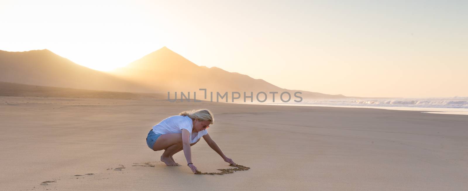 Lady drawing heart shape in sand on beach. by kasto