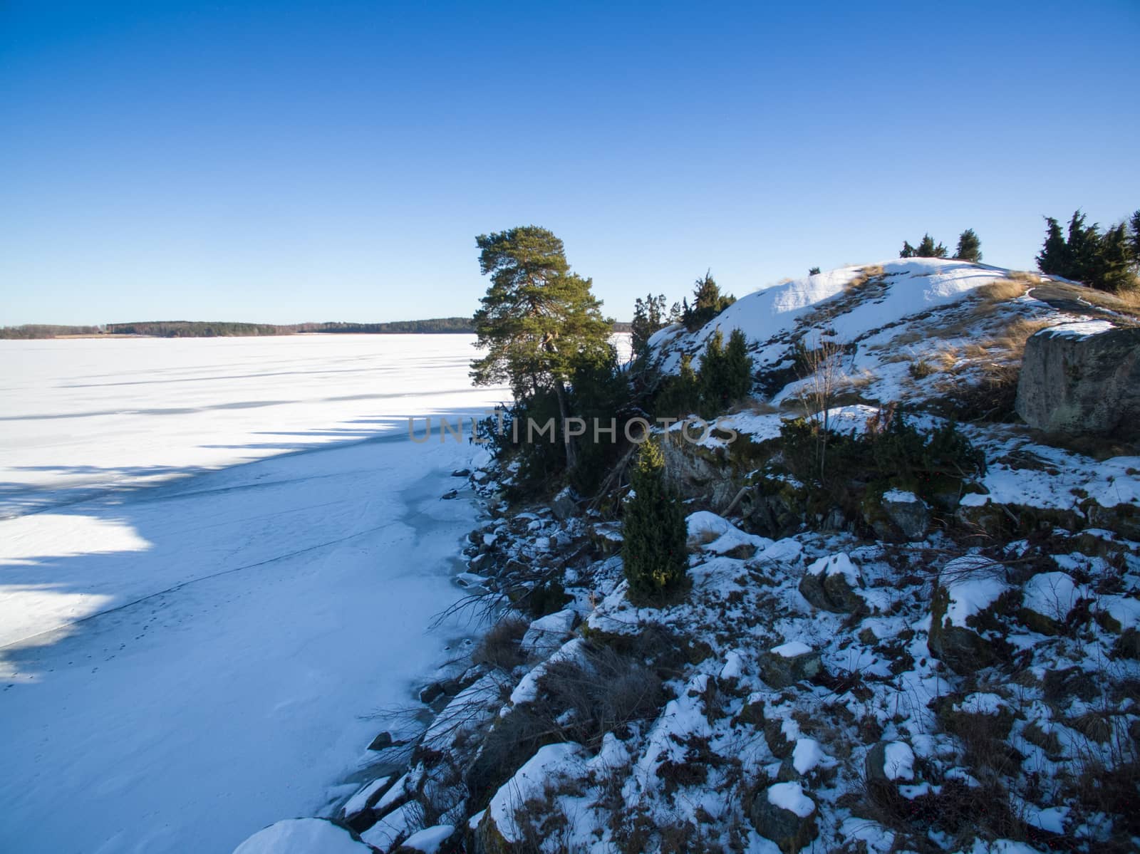 Long shadows on a frozen lake and rocky shore from the winter sun
