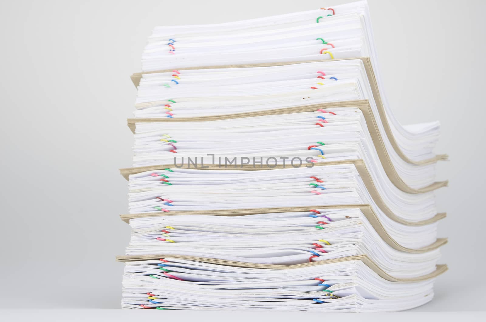 Overload of paperwork and brown envelope with colorful paperclip on white table.