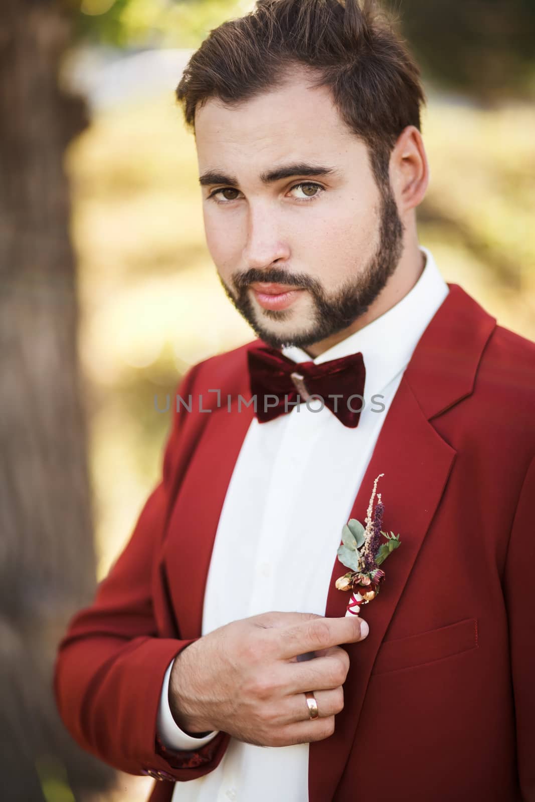 Portrait of the groom in a red suit with a bow tie, beard and mustache.