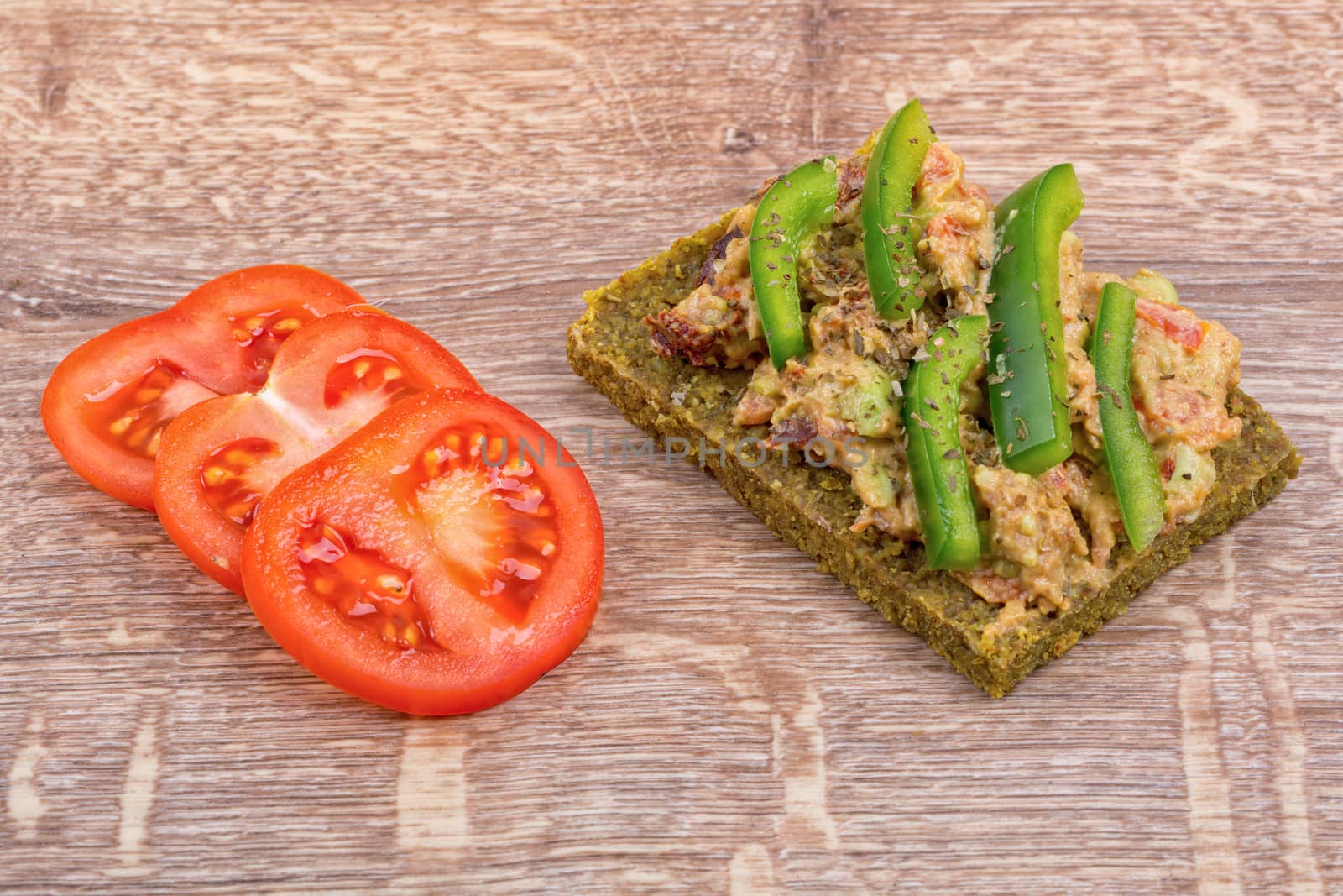 Raw bread with a spread decorated with green pepper and tomatoes