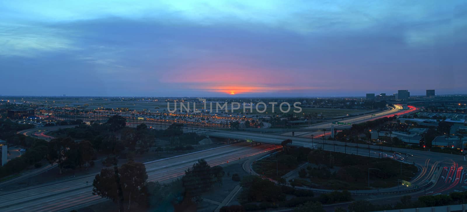 Aerial view of John Wayne Airport in Orange County, California, at sunset with rain in the air light trails across the 405 highway in front.
