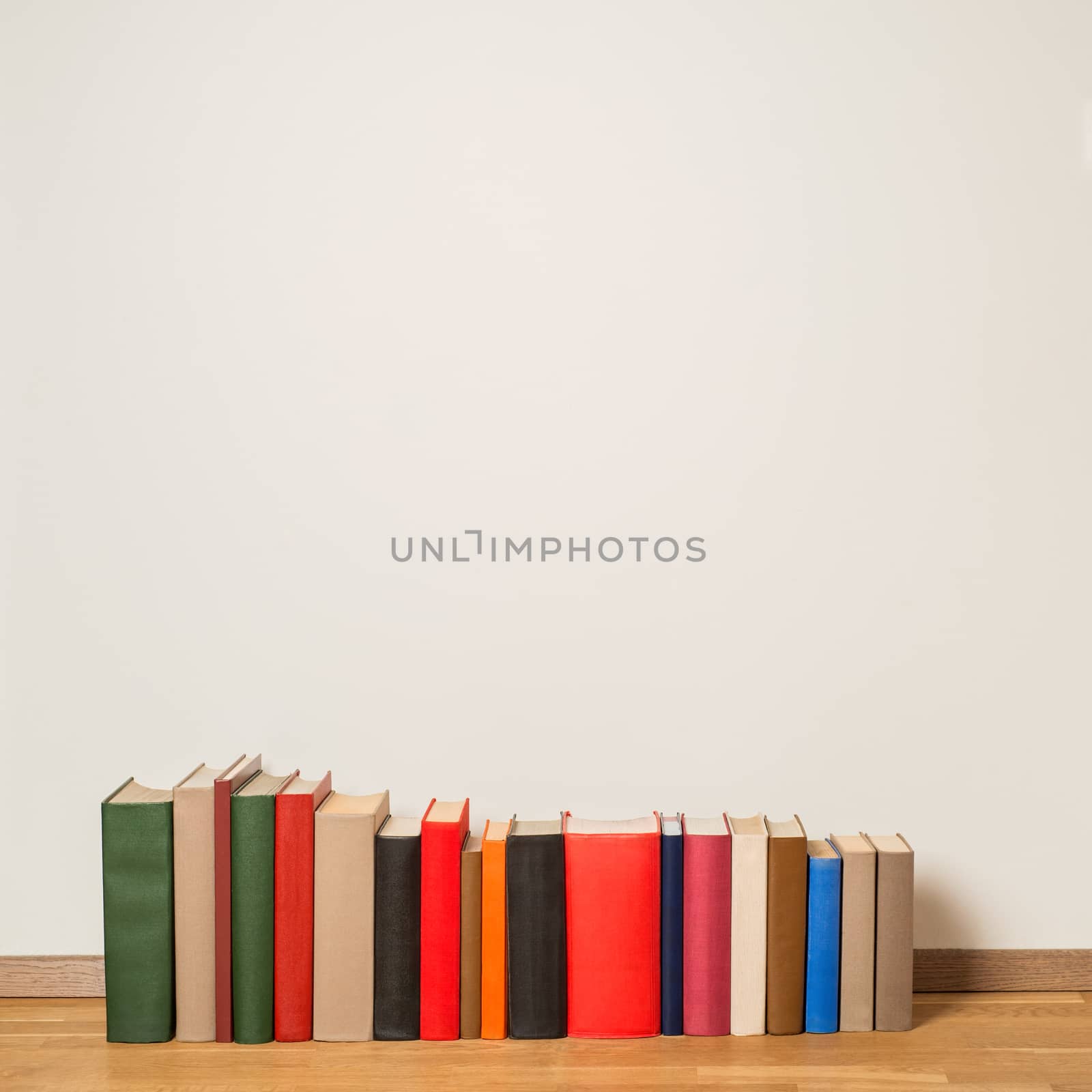 Old colorful books on wooden floor near the white wall