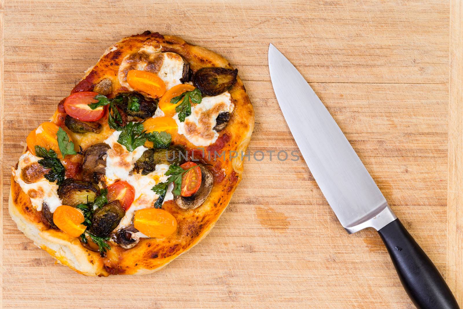 Freshly baked hand tossed vegetarian pizza with mushrooms, tomato and mozzarella cheese on a wooden cutting board alongside a kitchen knife