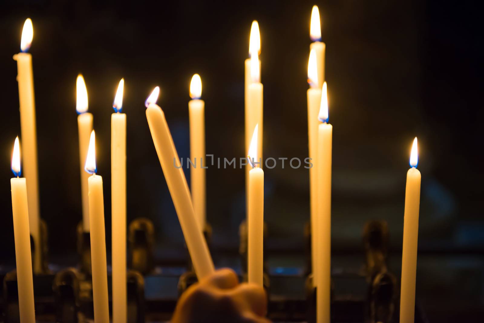 Hand lights candles in the church on the black background