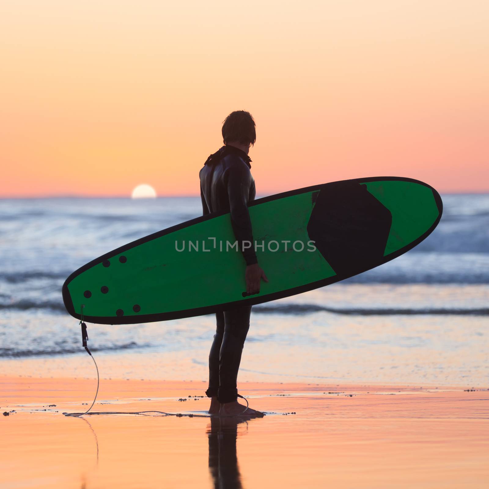 Silhouette of male surfer on the beach with the surfboard watching sunset.