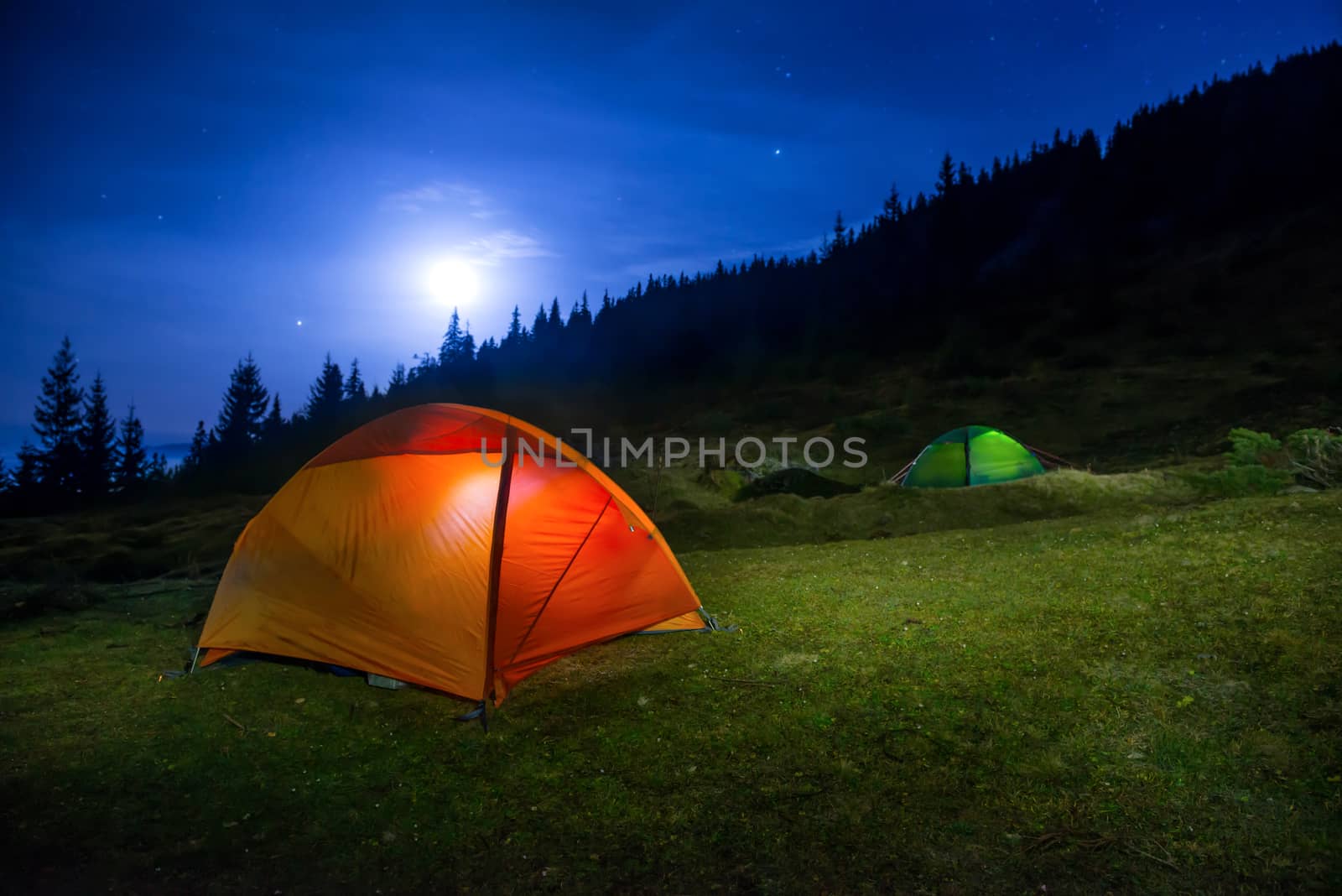 Two Illuminated orange and green camping tents under moon, stars at night