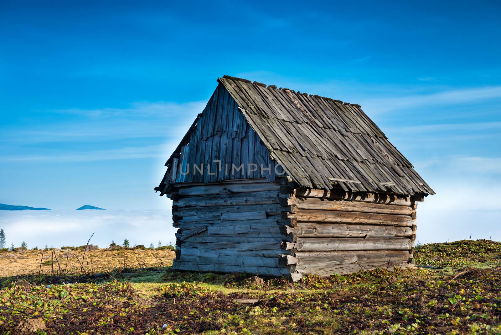 Old house in front of beautiful nature with clouds ocean, field of grass and mountains