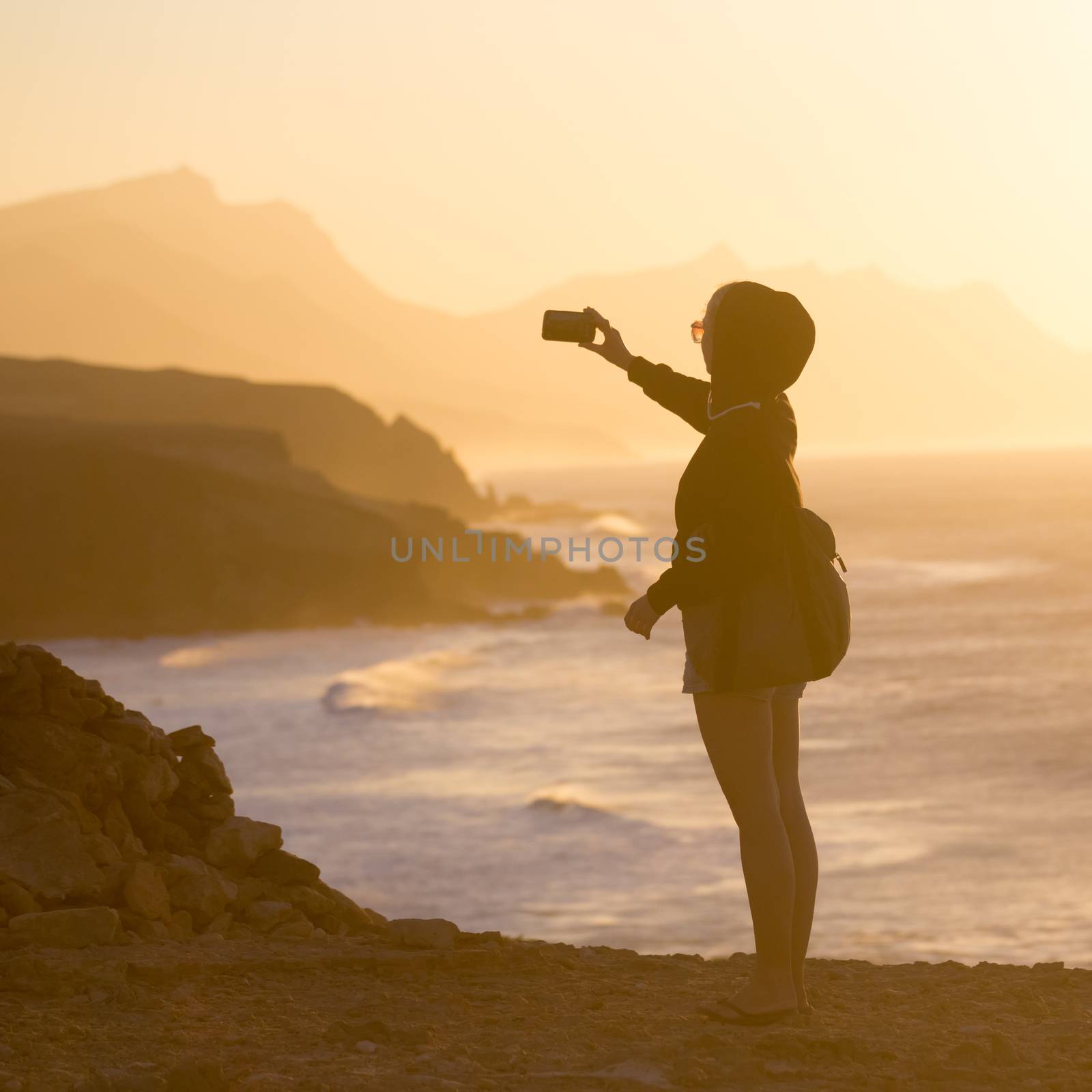 Woman snaping photo of La Pared beach in sunset. by kasto