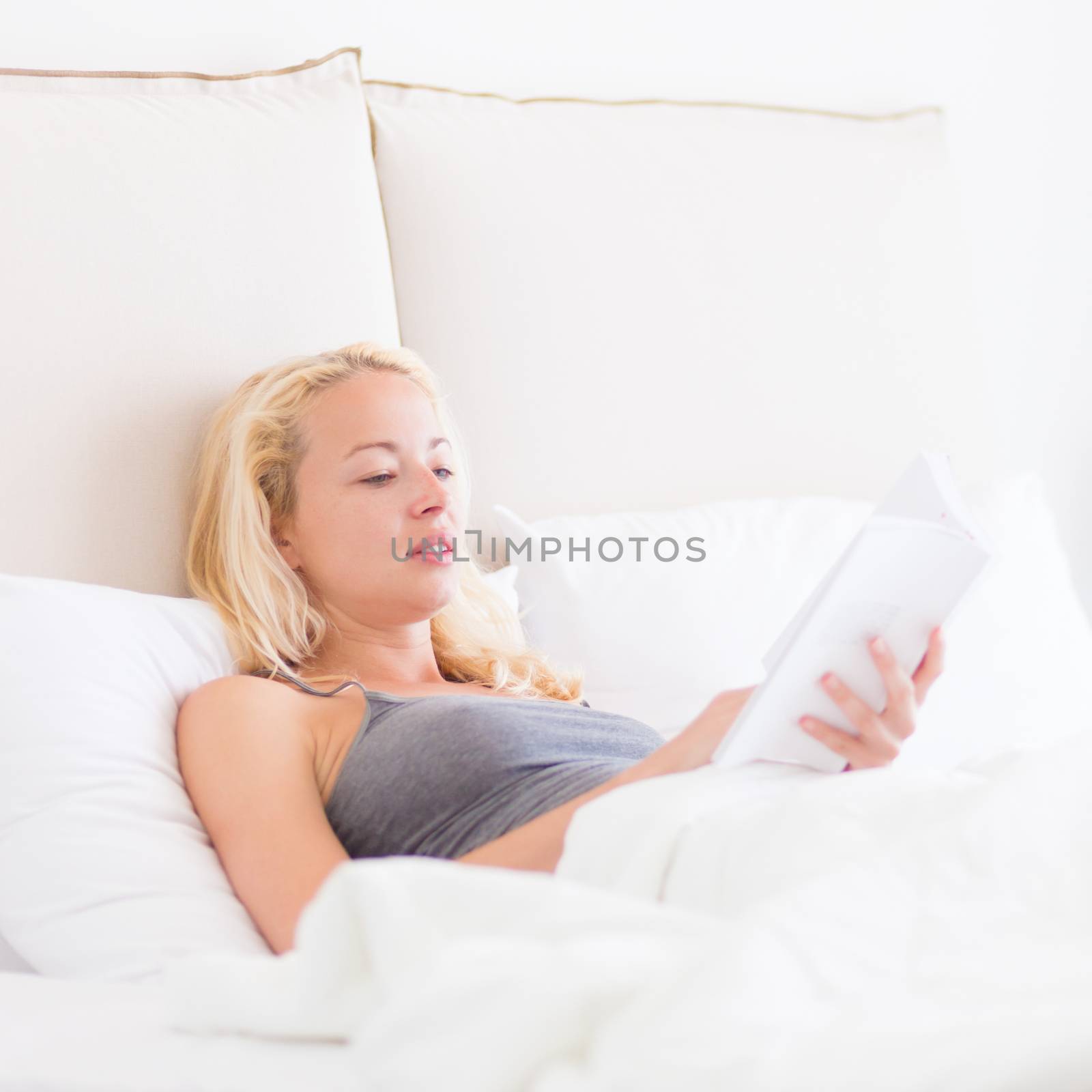 Young Caucasian woman reading book while lying in bed.