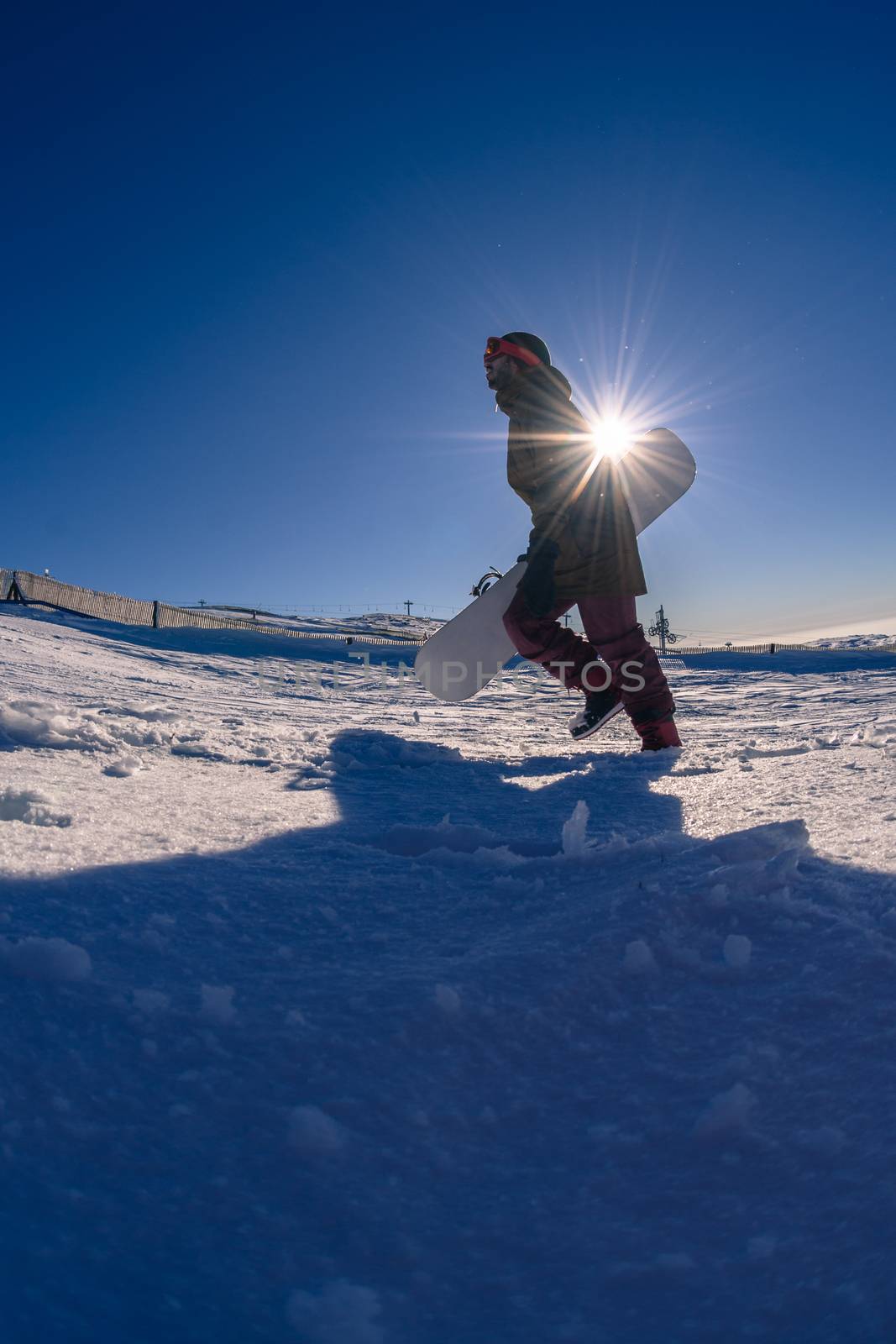 Snowboarder walking through deep fresh snow against blue sky.