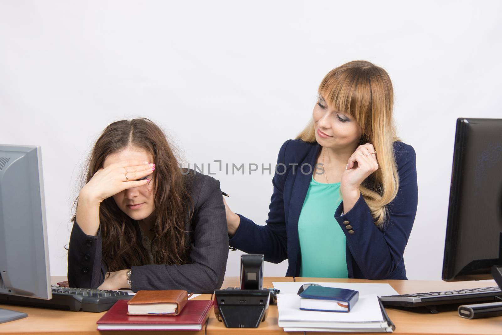 Two young beautiful girls colleagues sitting at the same desk in the office