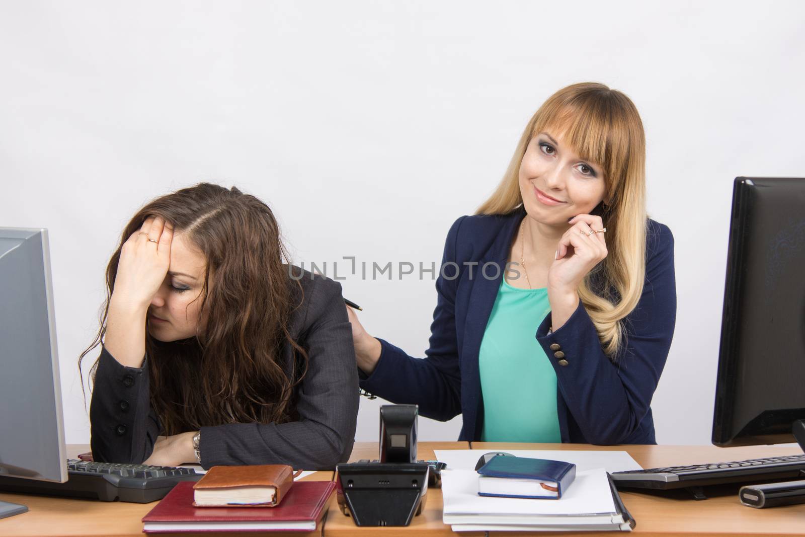 Two young beautiful girls colleagues sitting at the same desk in the office