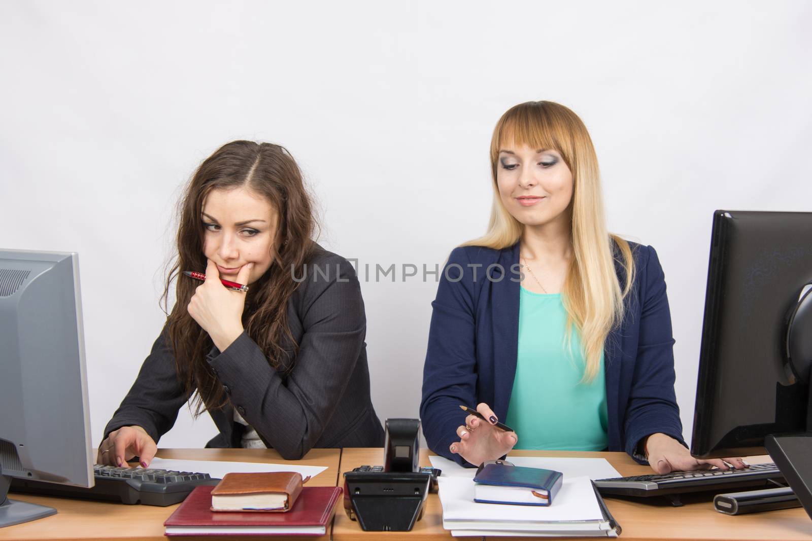 Two young beautiful girls colleagues sitting at the same desk in the office