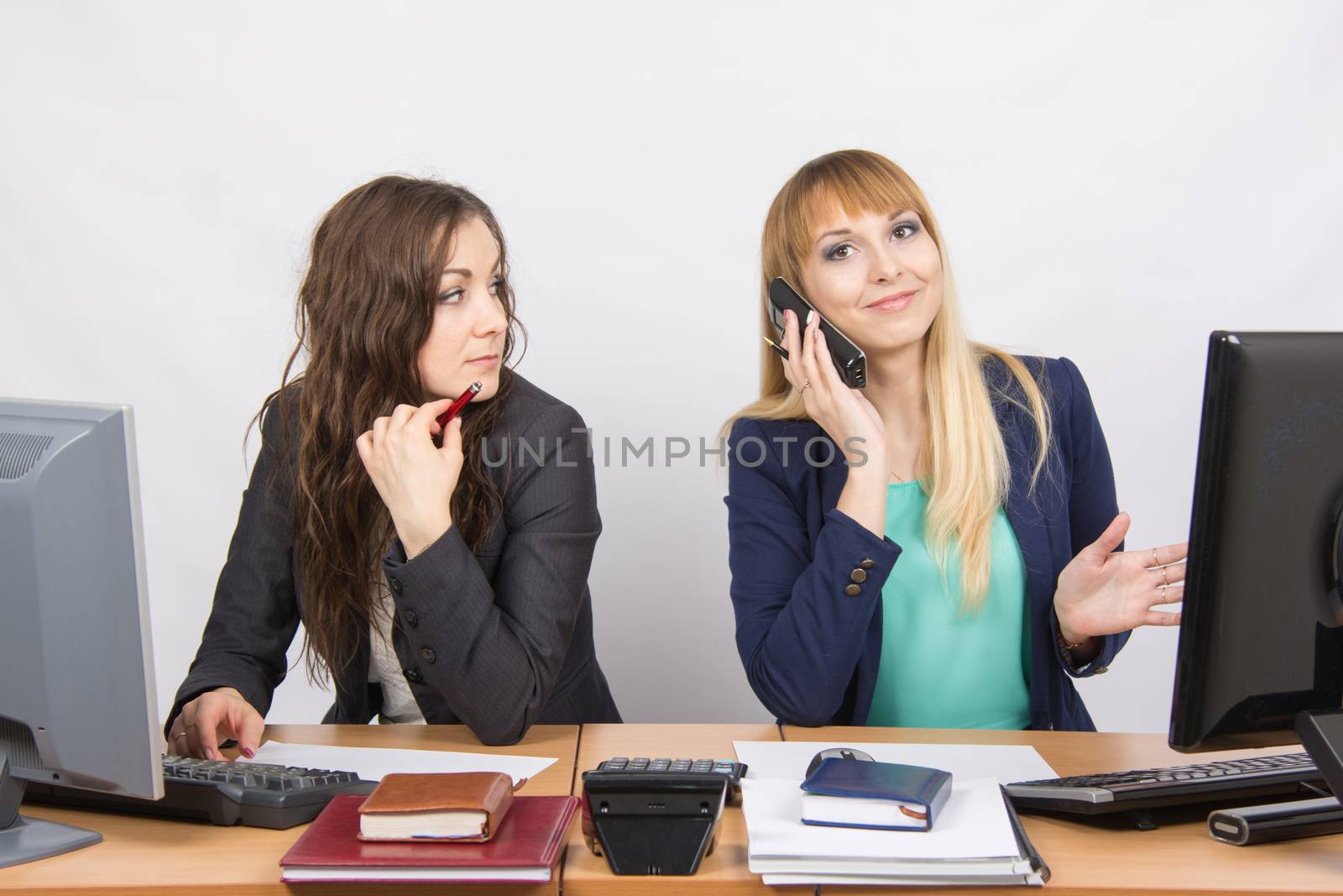 Two young beautiful girls colleagues sitting at the same desk in the office