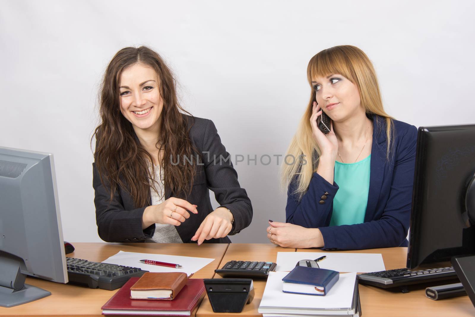 Two young beautiful girls colleagues sitting at the same desk in the office