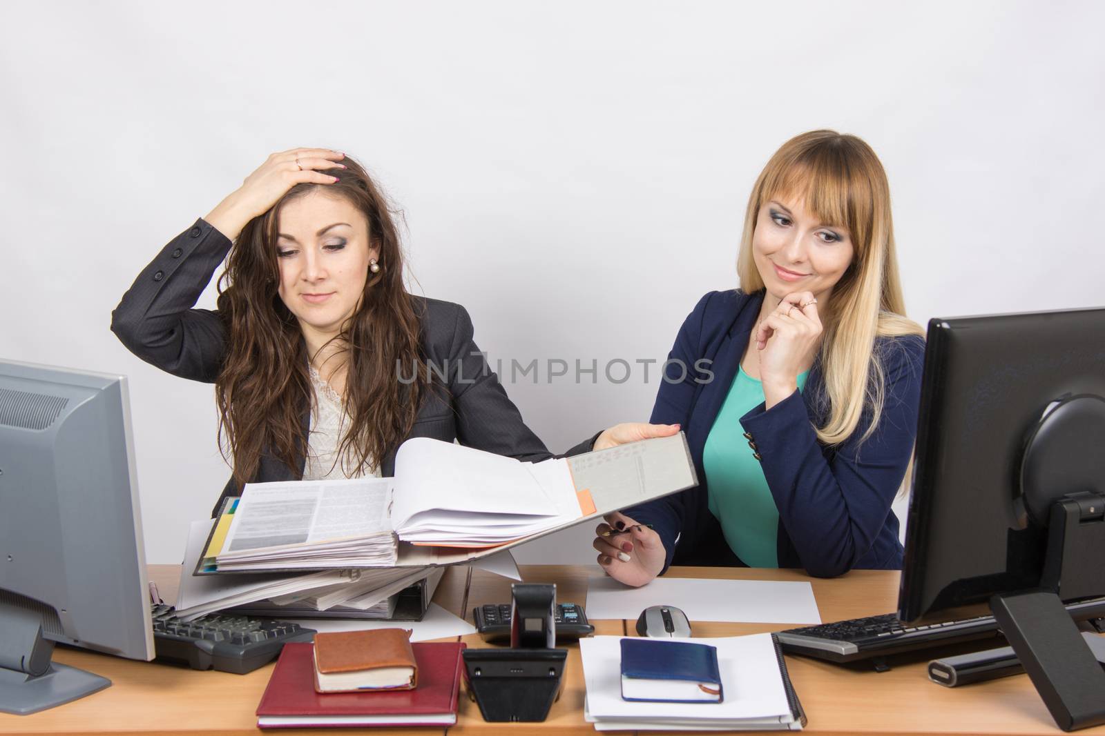Two young beautiful girls colleagues sitting at the same desk in the office