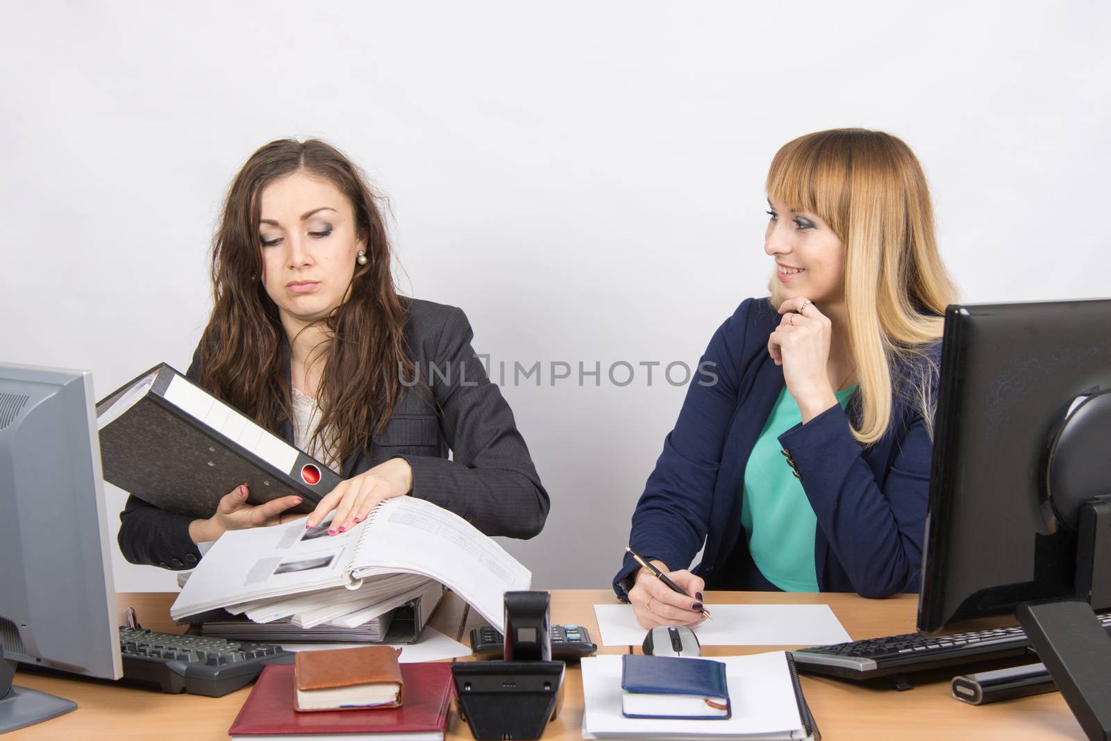 Two young beautiful girls colleagues sitting at the same desk in the office