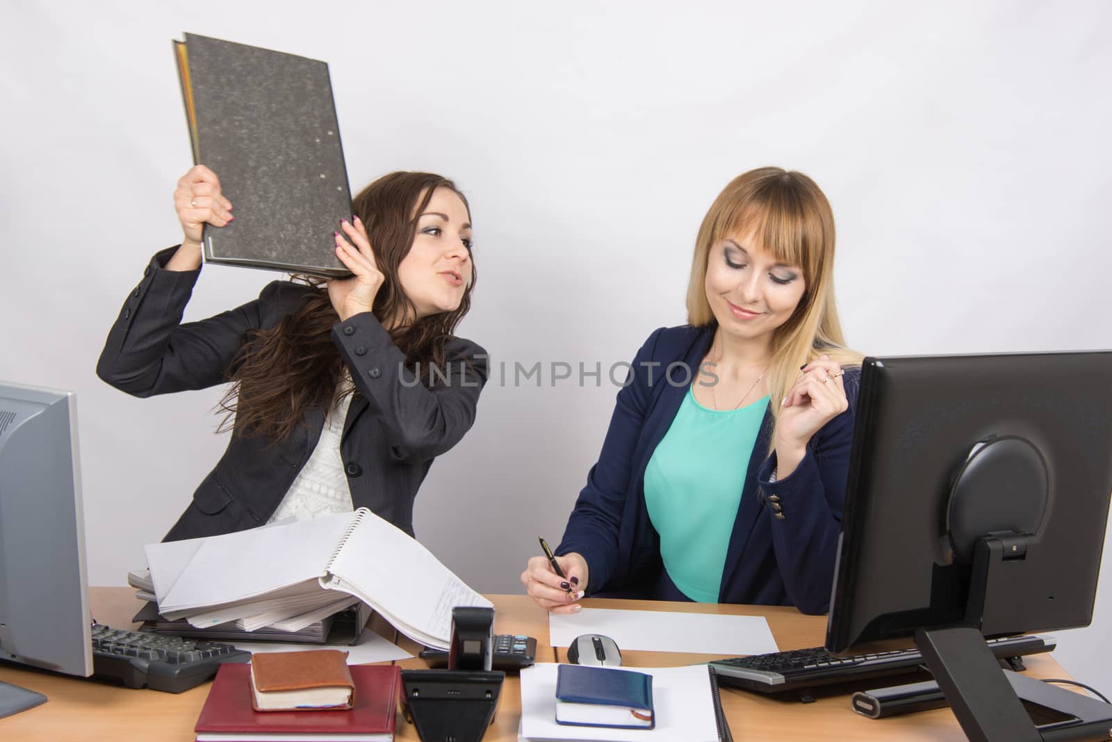 Two young beautiful girls colleagues sitting at the same desk in the office
