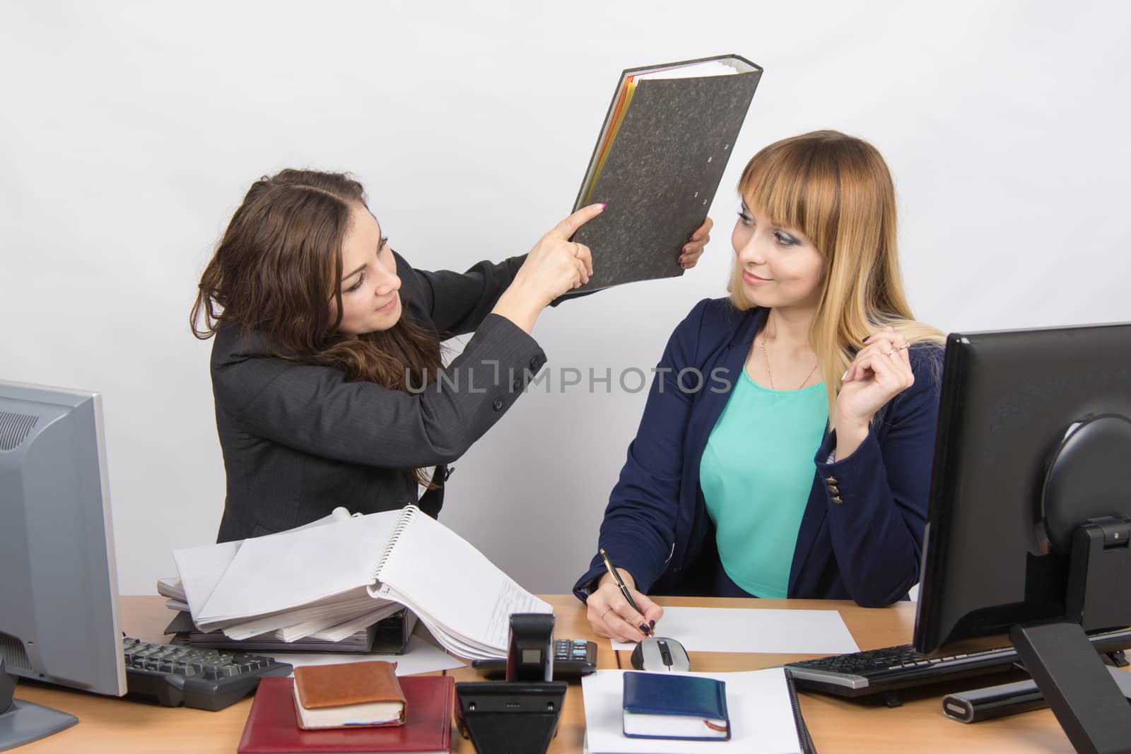 Two young beautiful girls colleagues sitting at the same desk in the office