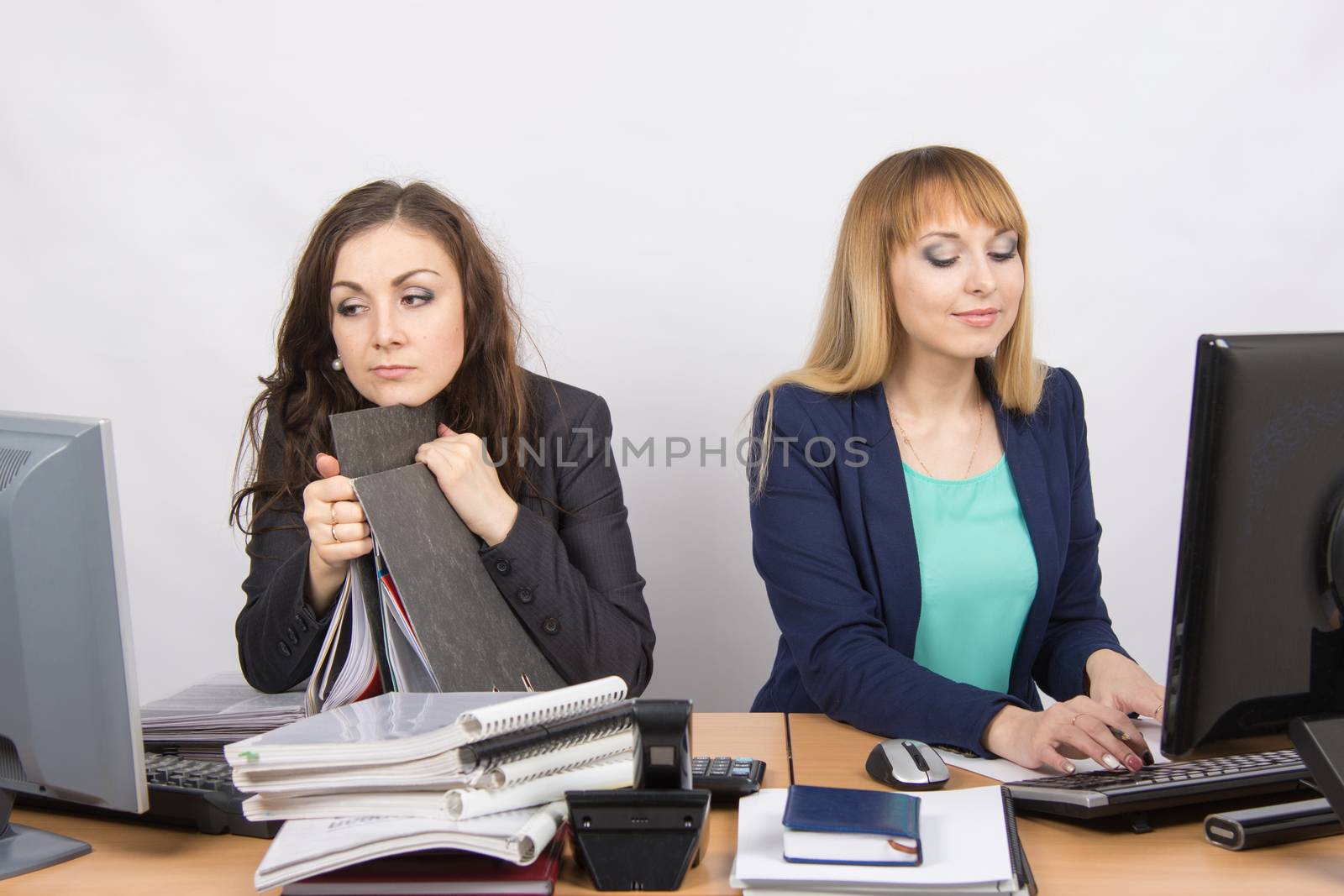 Two young beautiful girls colleagues sitting at the same desk in the office