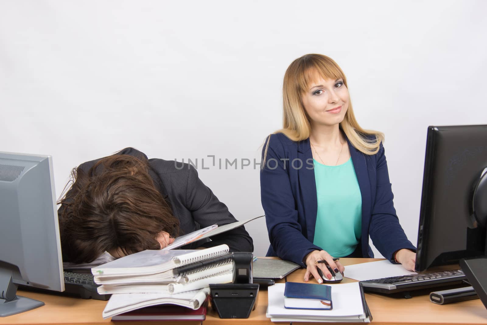 Two young beautiful girls colleagues sitting at the same desk in the office