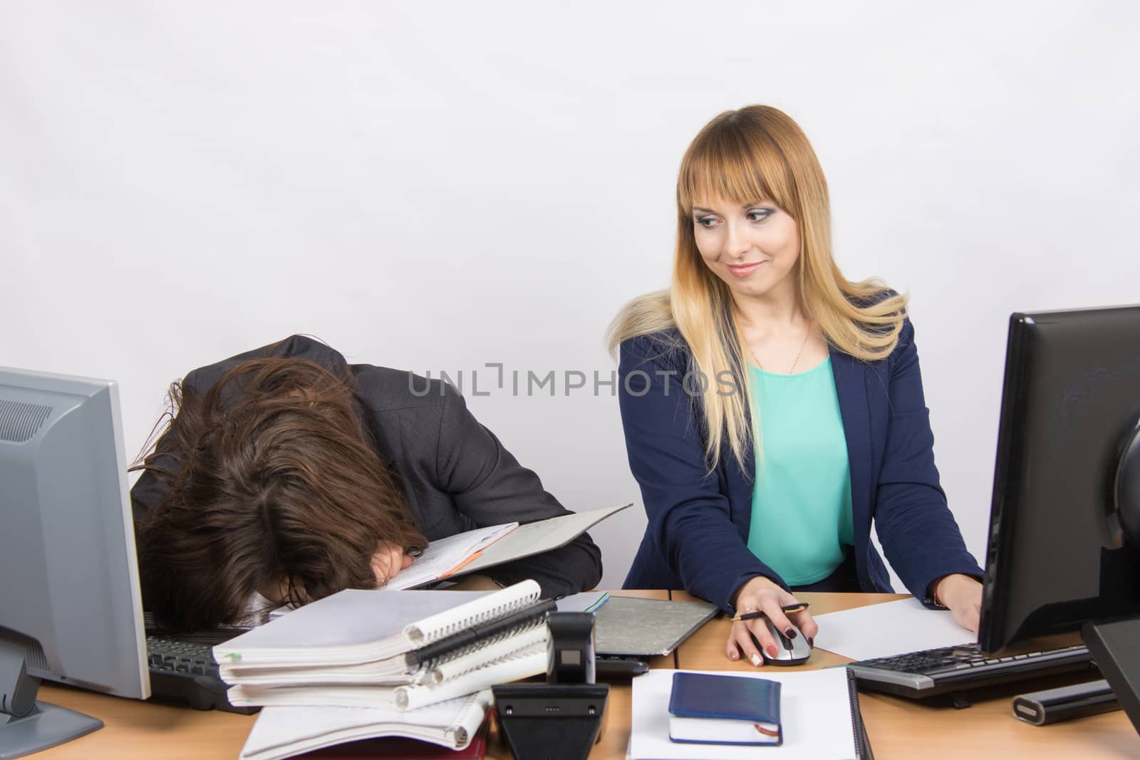 Two young beautiful girls colleagues sitting at the same desk in the office