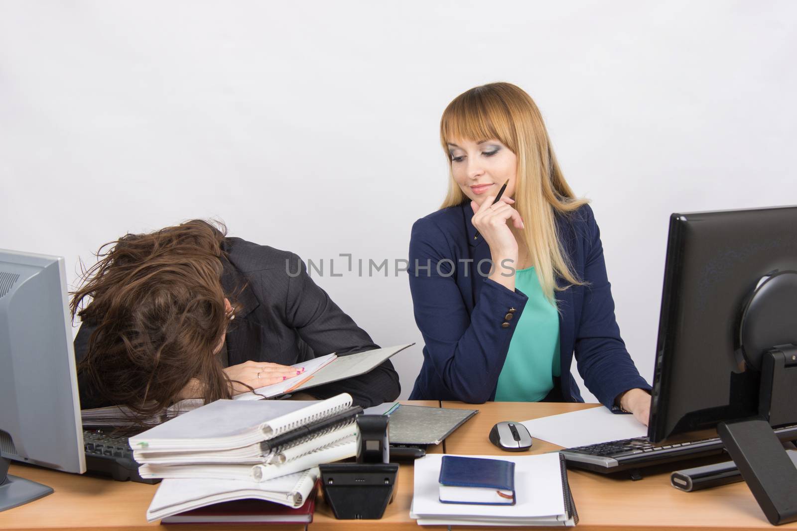 Two young beautiful girls colleagues sitting at the same desk in the office