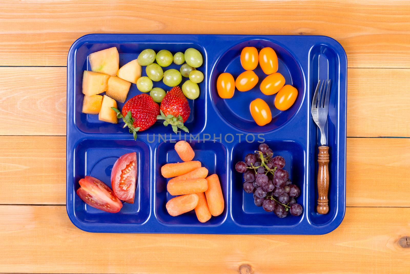 Delicious tangy and sweet fruit sampler of melon, grapes, tomatoes, carrots and grapes in lunch tray with fork