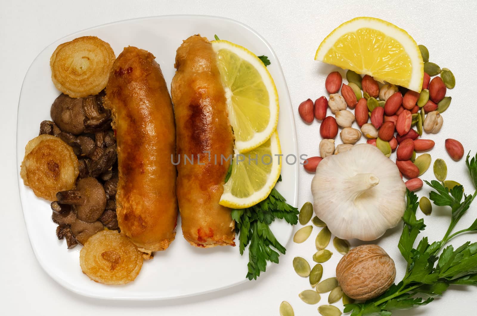 Fried sausage with mushrooms, lemon, parsley and onions on a white background. Cleaned peanuts and pumpkin seeds, head of garlic, lay in a heap.