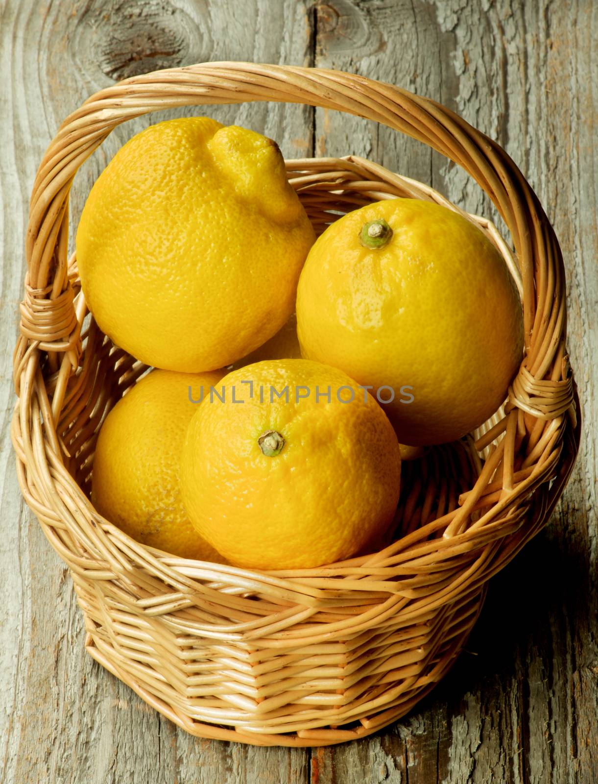Heap of Raw Ripe Lemons in Wicker Basket closeup on Rustic Wooden background