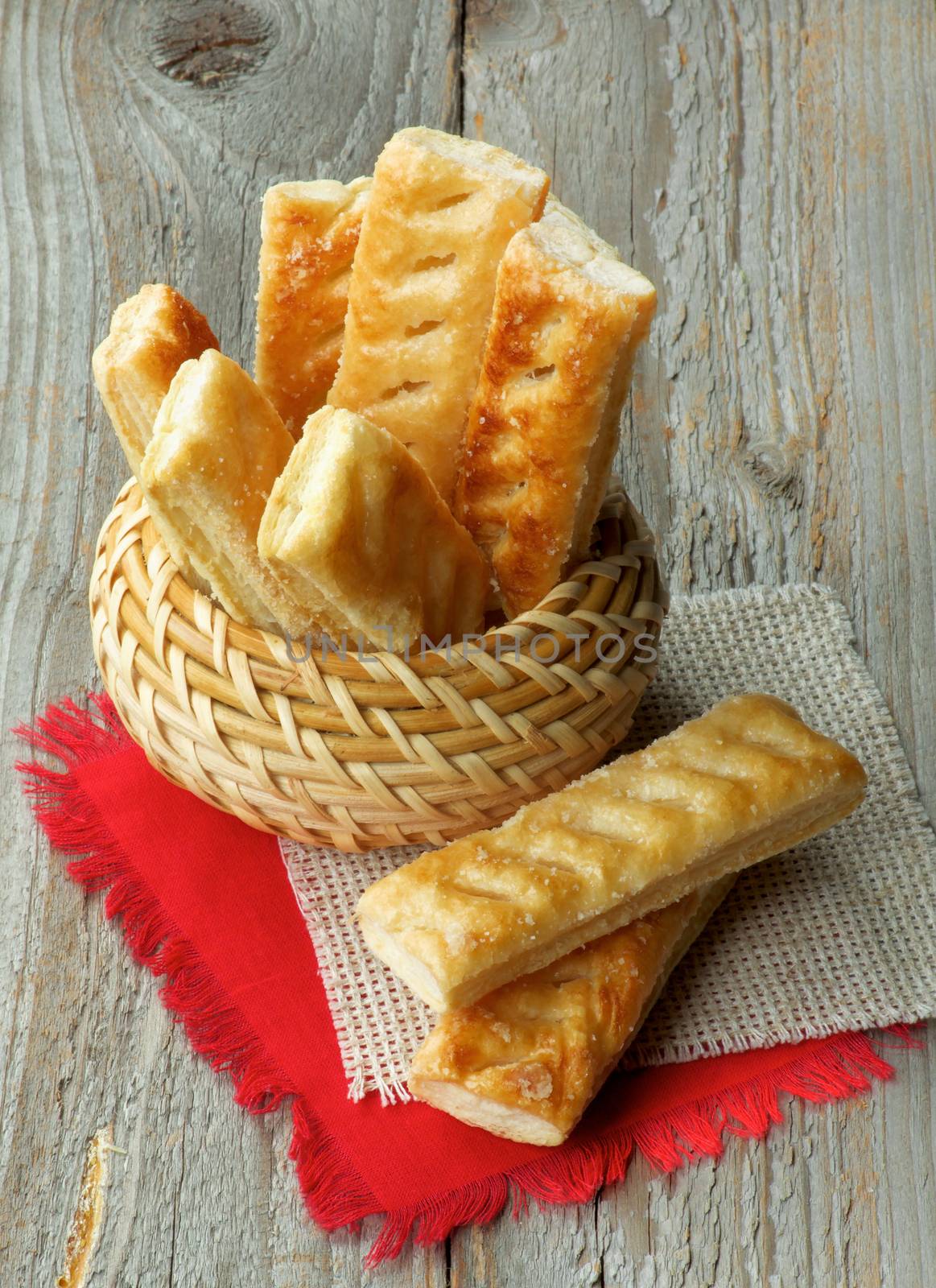 Puff Pastry Sticks Sprinkled with Sugar Crystals in Wicker Bowl and Napkins closeup on Wooden background
