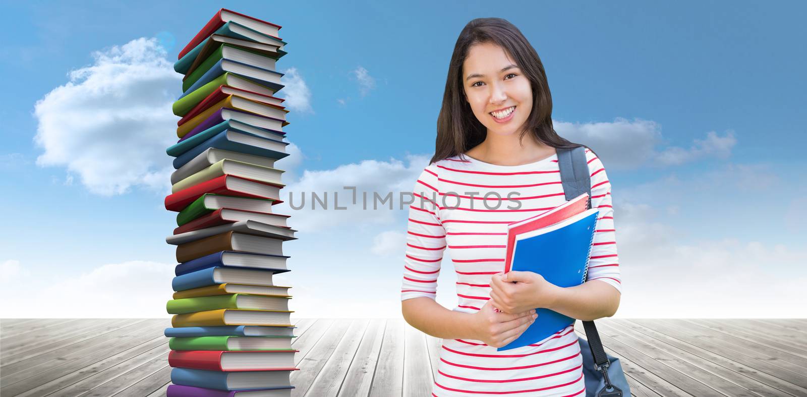 College girl holding books with blurred students in park against stack of books against sky