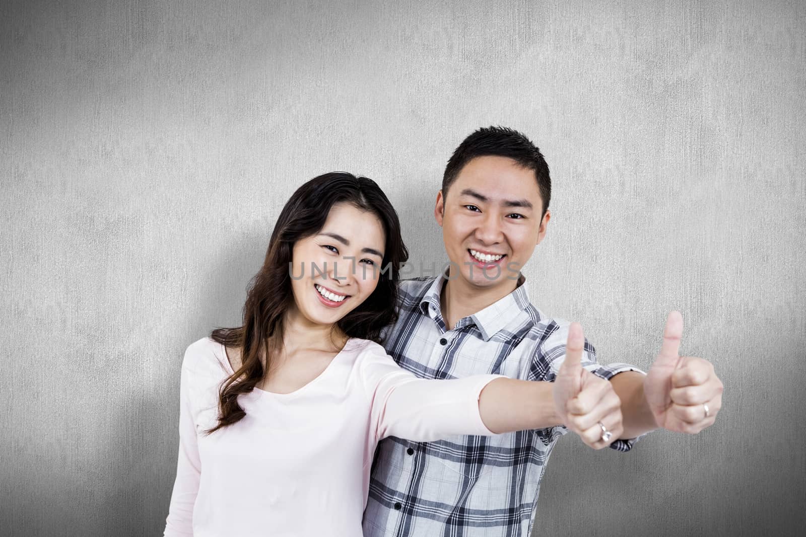 Couple showing thumbs up while standing  against white and grey background