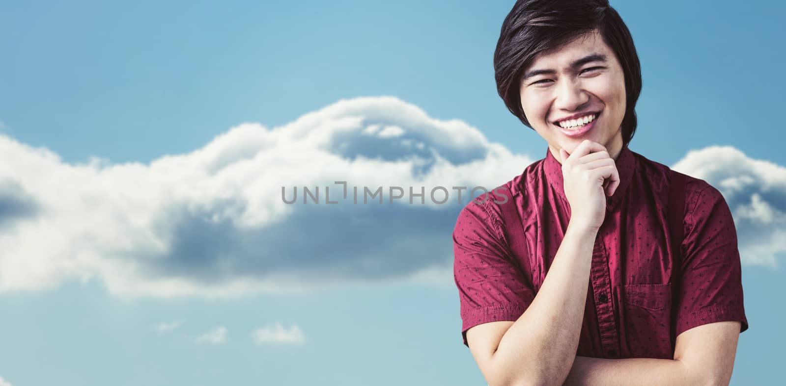 Smiling hipster holding his chin against bright blue sky with cloud