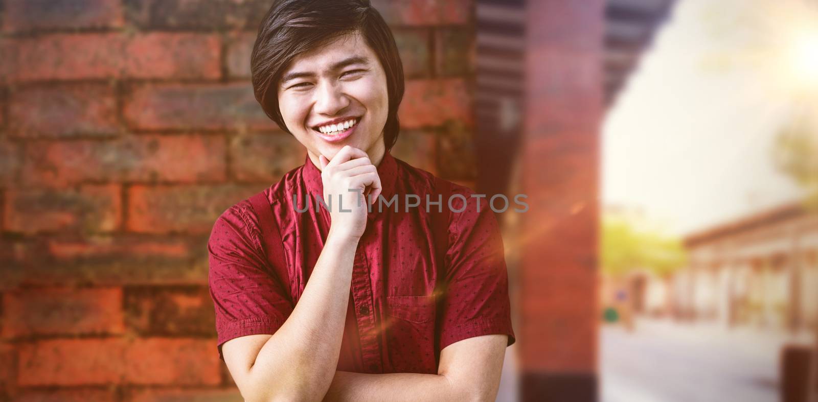 Smiling hipster holding his chin against view of brick wall