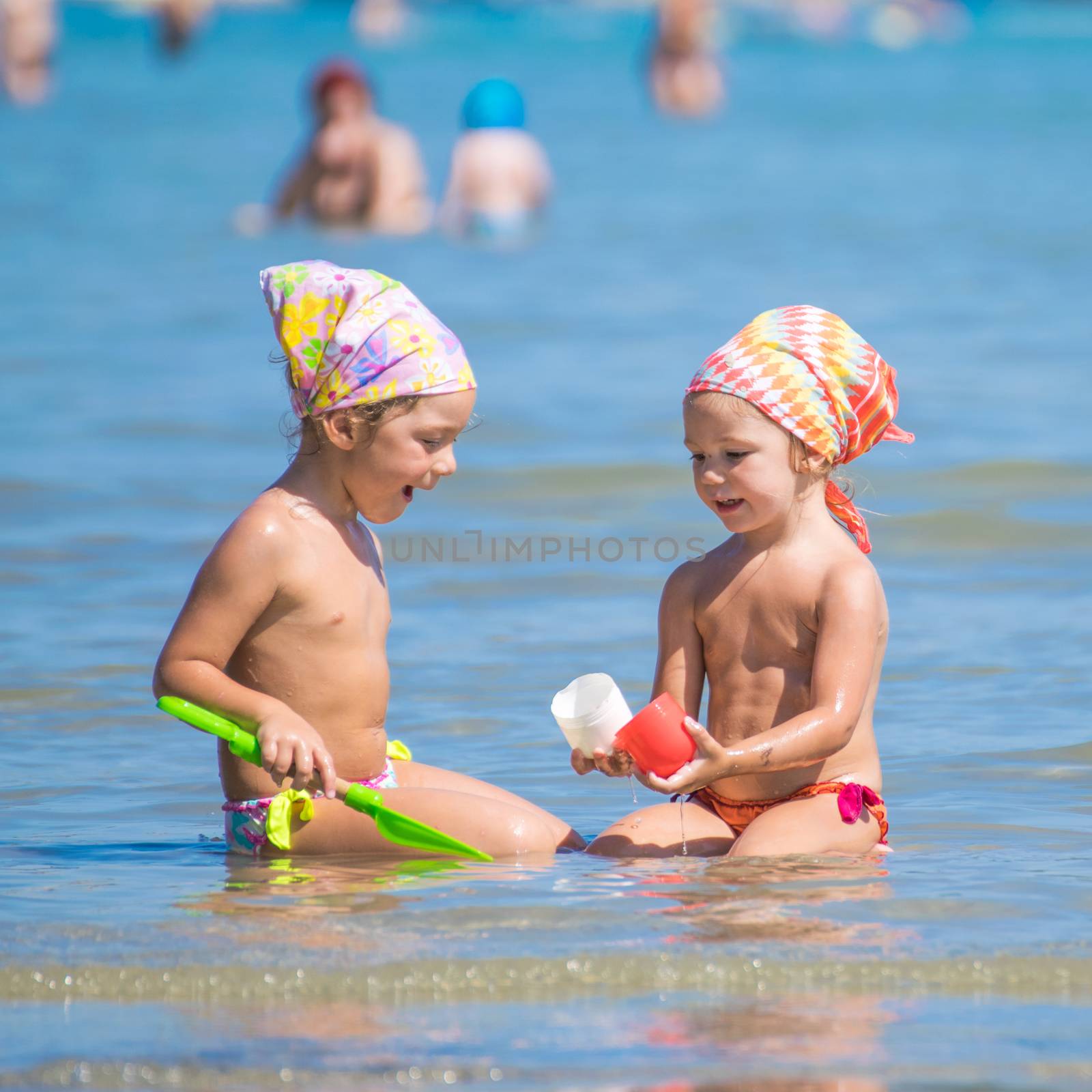 Two little girls with colored bandana playing in the sea.