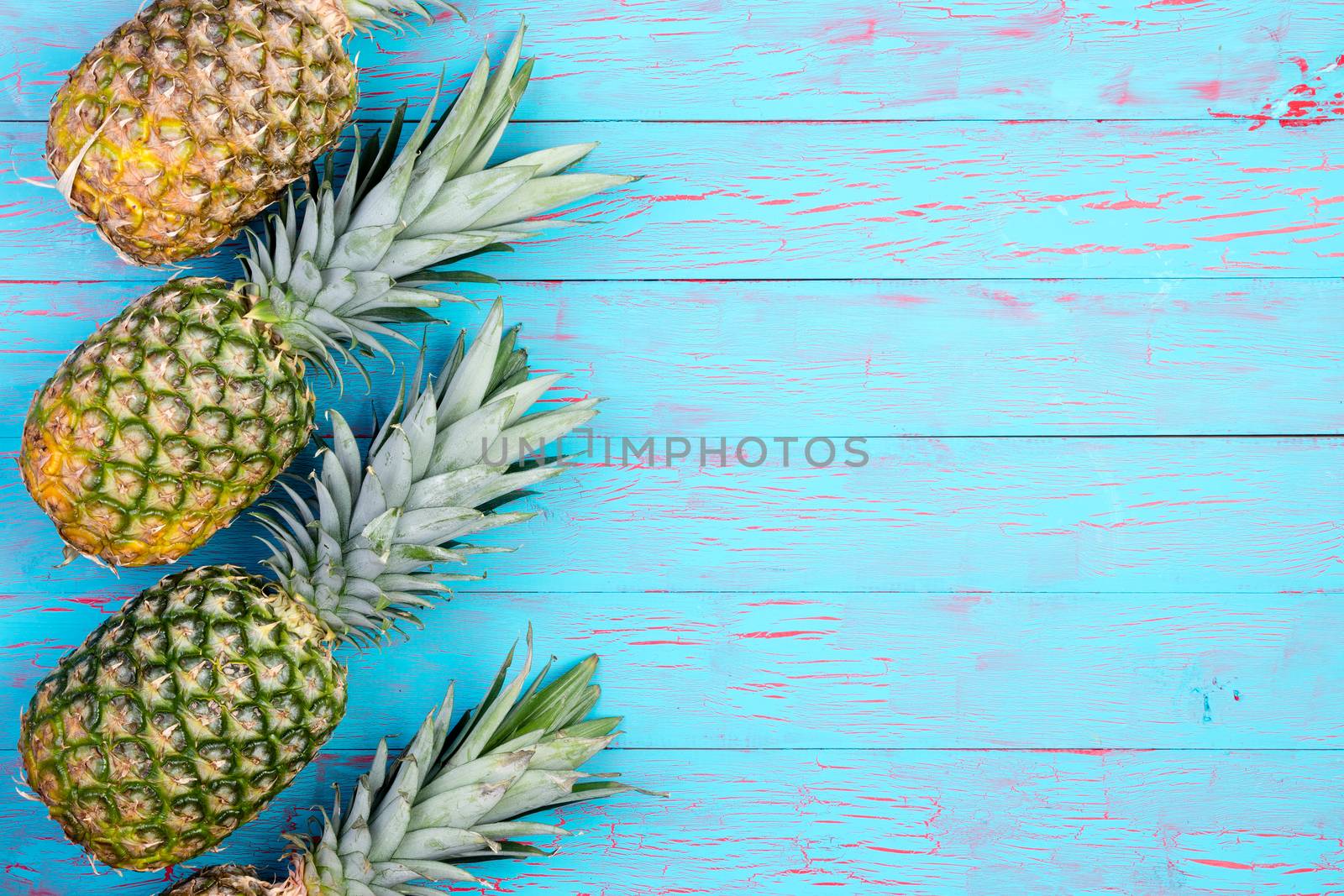 Row of four slanted pineapple fruits laid down on old blue wooden floor or table with copy space