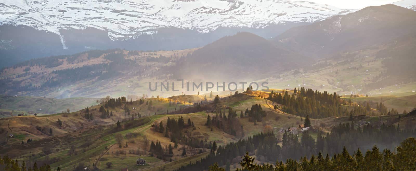 Evening light in spring carpathian mountains. Snow and green fields