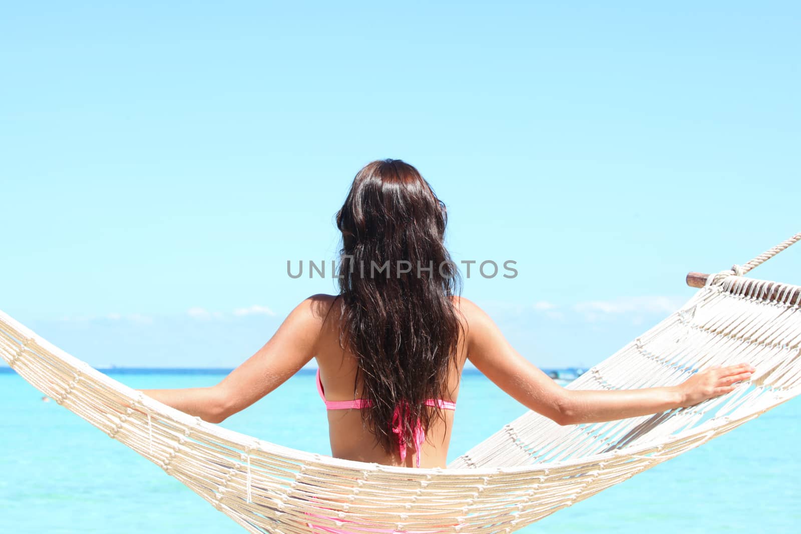 Rear view of a woman in bikini sitting on a hammock on a beach by the sea