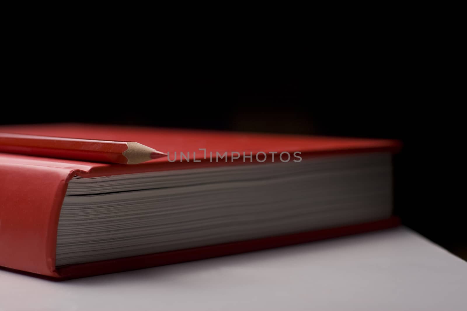 Horizontal side view of a red closed book with a red pencil on top of it