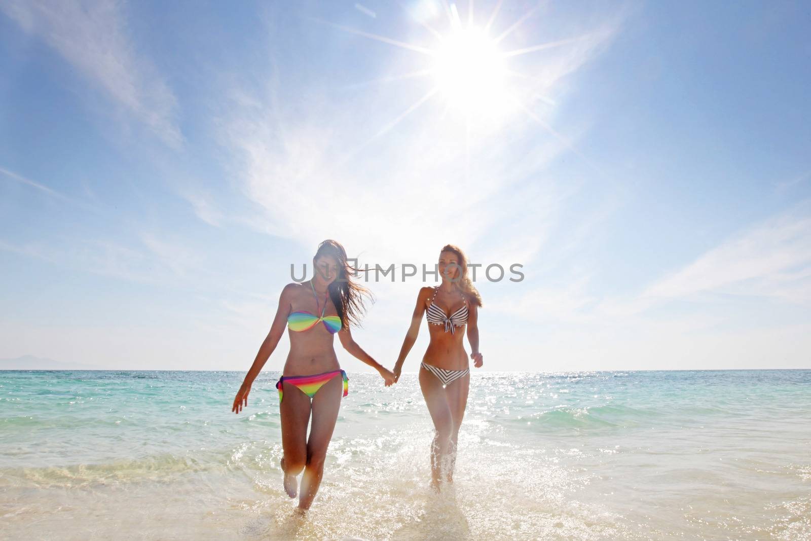 Two smiling women in bikini walking from sea to beach