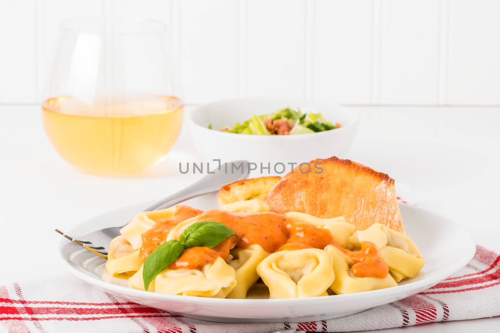 Tortelloni with caesar salad and white wine.  Useful for menus and other food service applications.