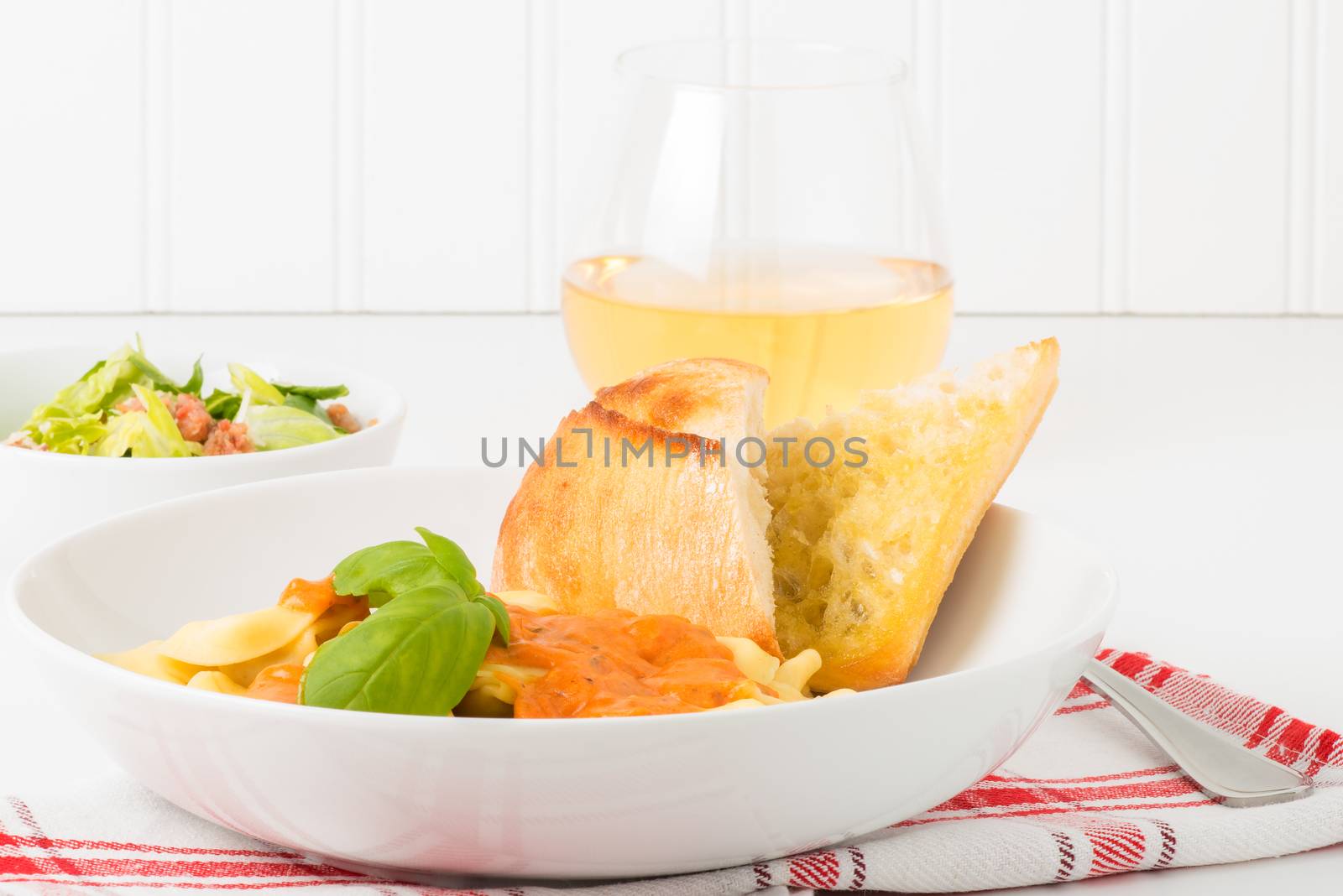 Bowl of tortelloni with caesar salad and wine.  Useful for a menu or other food service promotional materials.