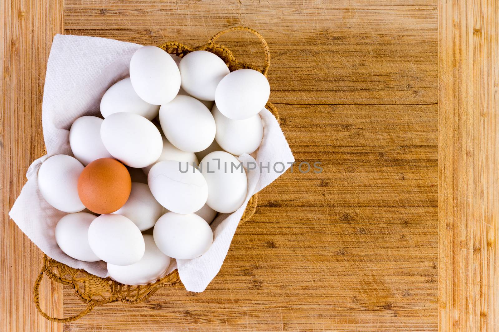 Single wicker filled with single brown egg on top of white ones over wooden table background with copy space