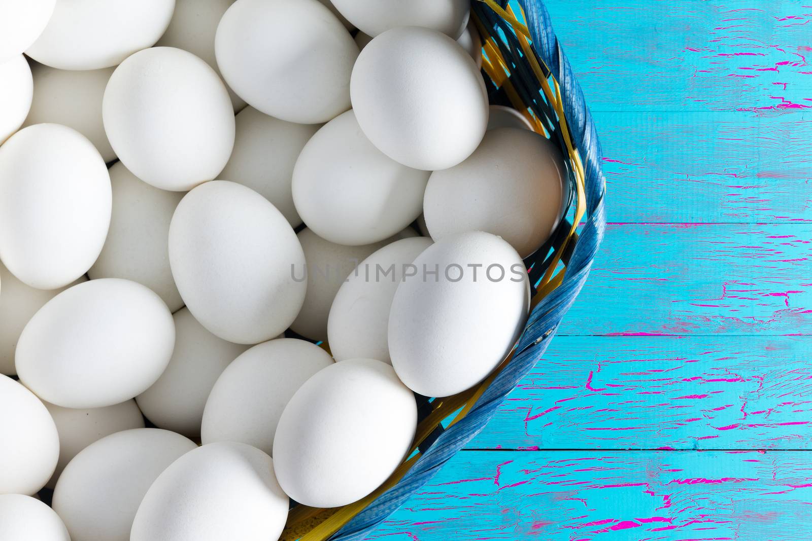 Wicker basket full of farm fresh clean white hens eggs on a wooden table painted with exotic blue crackle paint with copy space