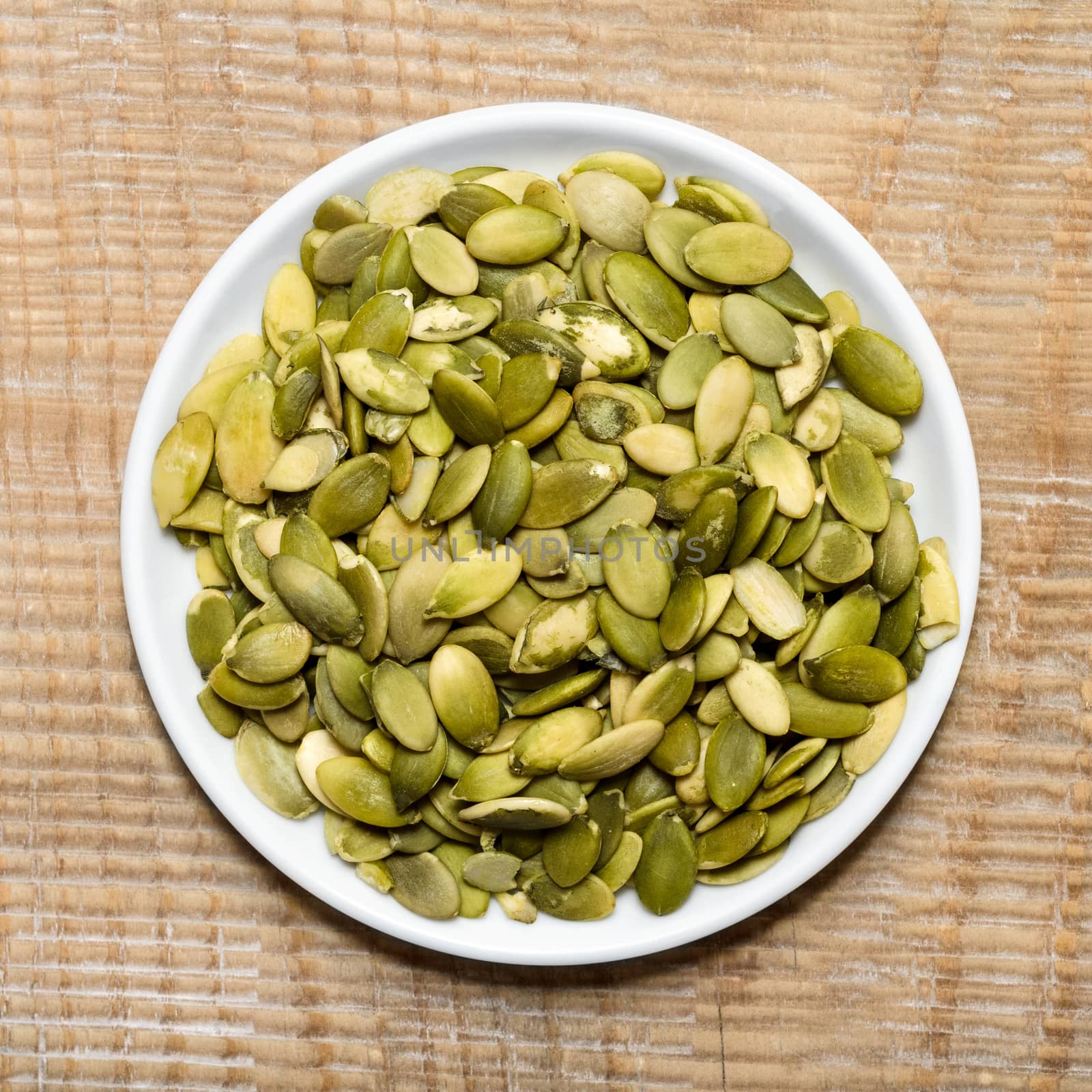 Pumpkin seeds in the plate, on wooden background by Gaina