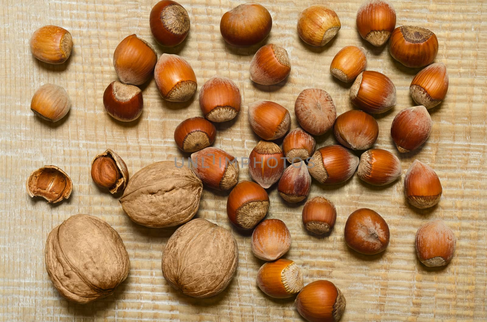 Hazelnuts and walnuts are scattered on wooden background.